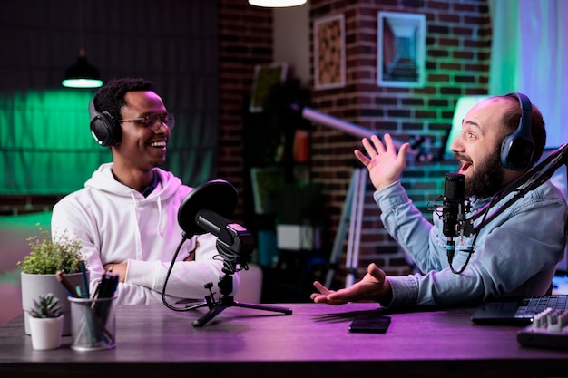 Pov of male bloggers vlogging podcast talk on camera, using streaming equipment in studio with neon lights. content creators having fun filming online episode for social media.