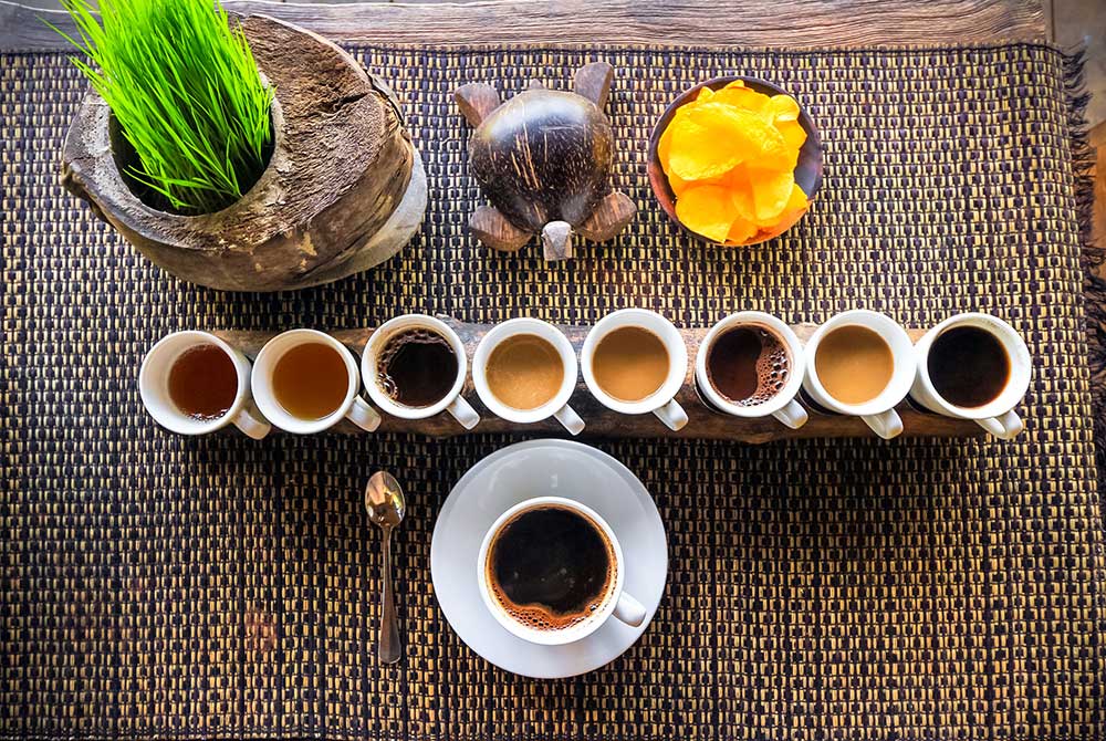 A flight of Bali coffee cups on a woven mat with fresh fruit
