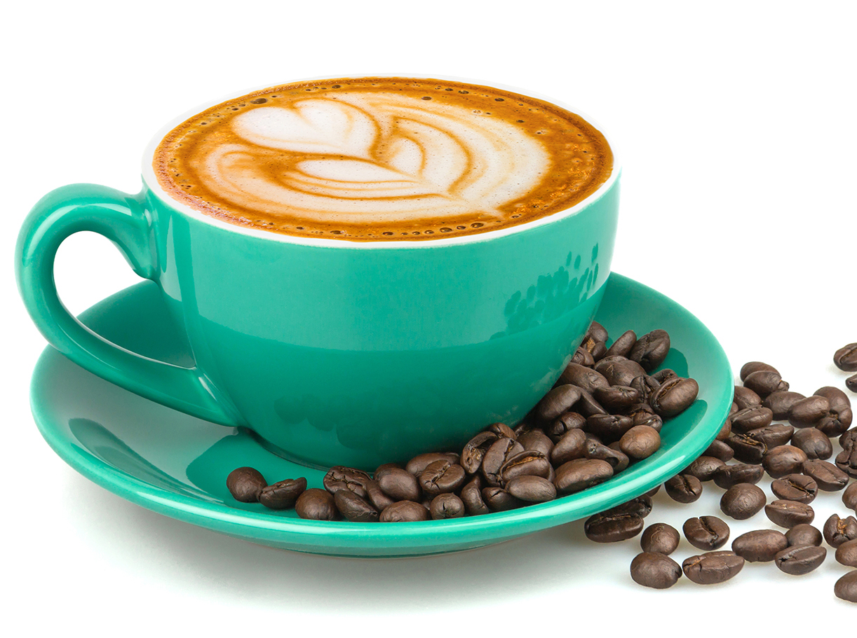 A latte with heart art in a teal cup surrounded by roasted coffee beans