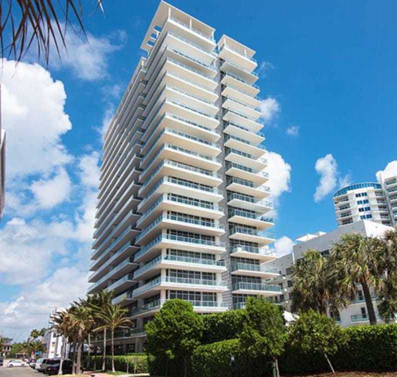 A modern white condominium building framed by palms