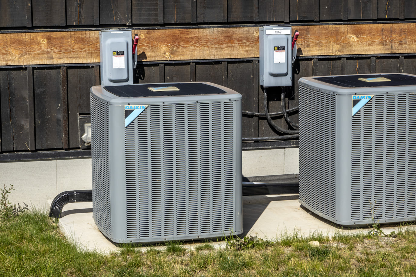 Two Daikin outdoor air conditioning condensers installed side by side on a concrete pad beside a home