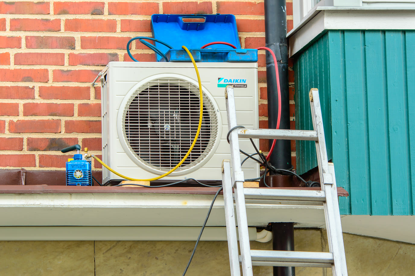 New Daikin outdoor unit being installed on the brick wall of a home