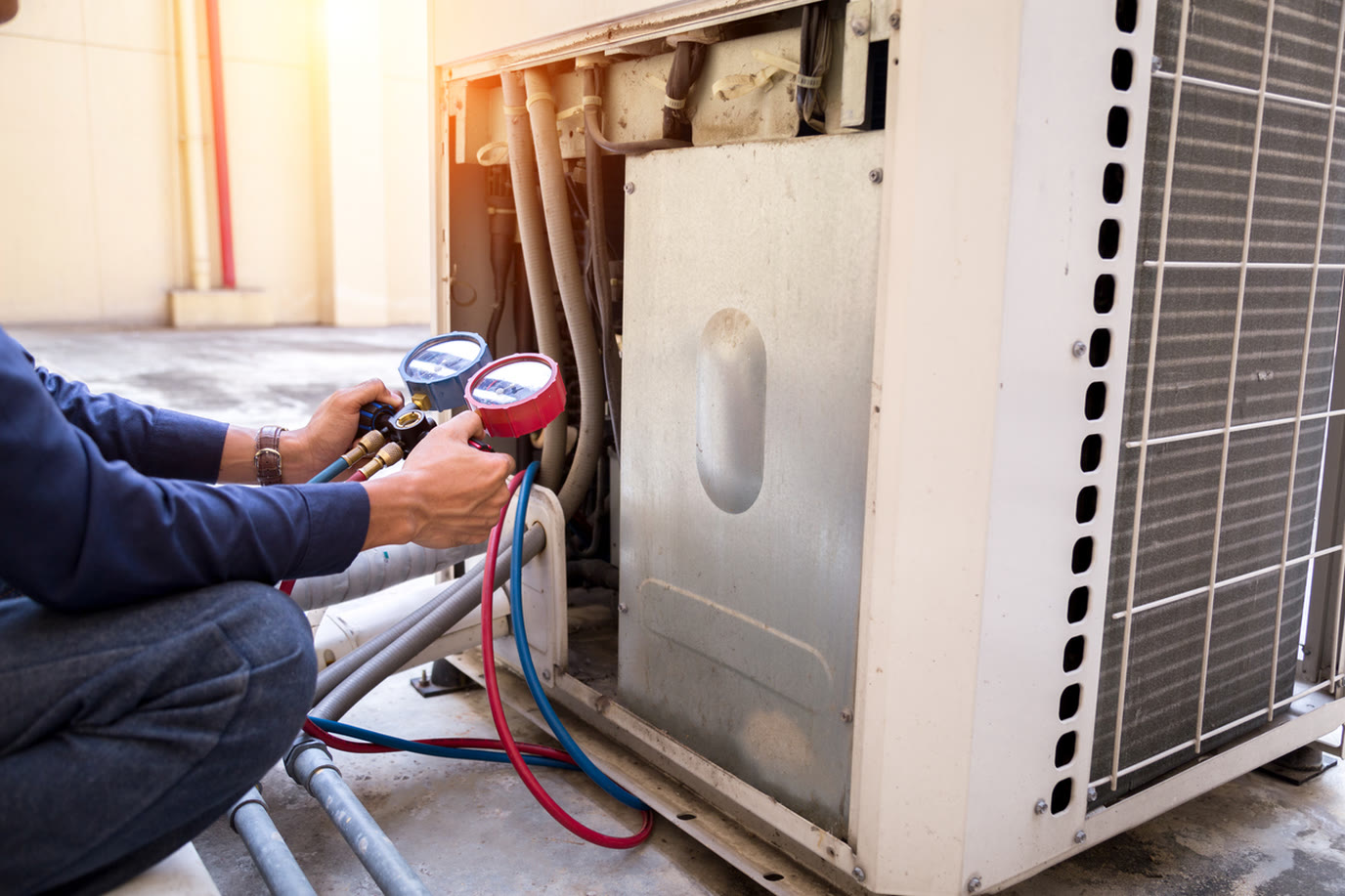 Technician checking refrigerant pressure on an outdoor air conditioning unit with a gauge manifold