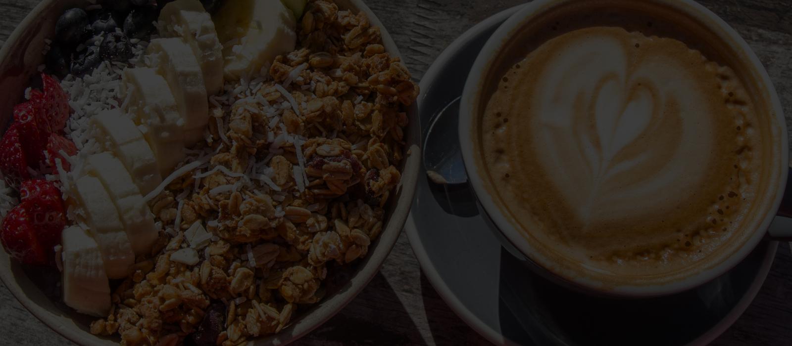 A latte beside a bowl of granola