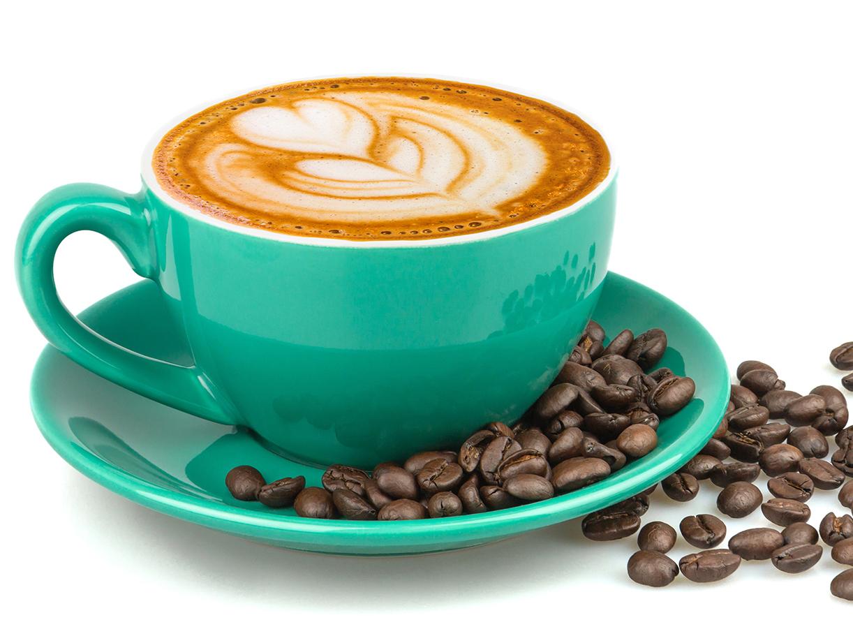 A latte with heart art in a teal cup surrounded by roasted coffee beans