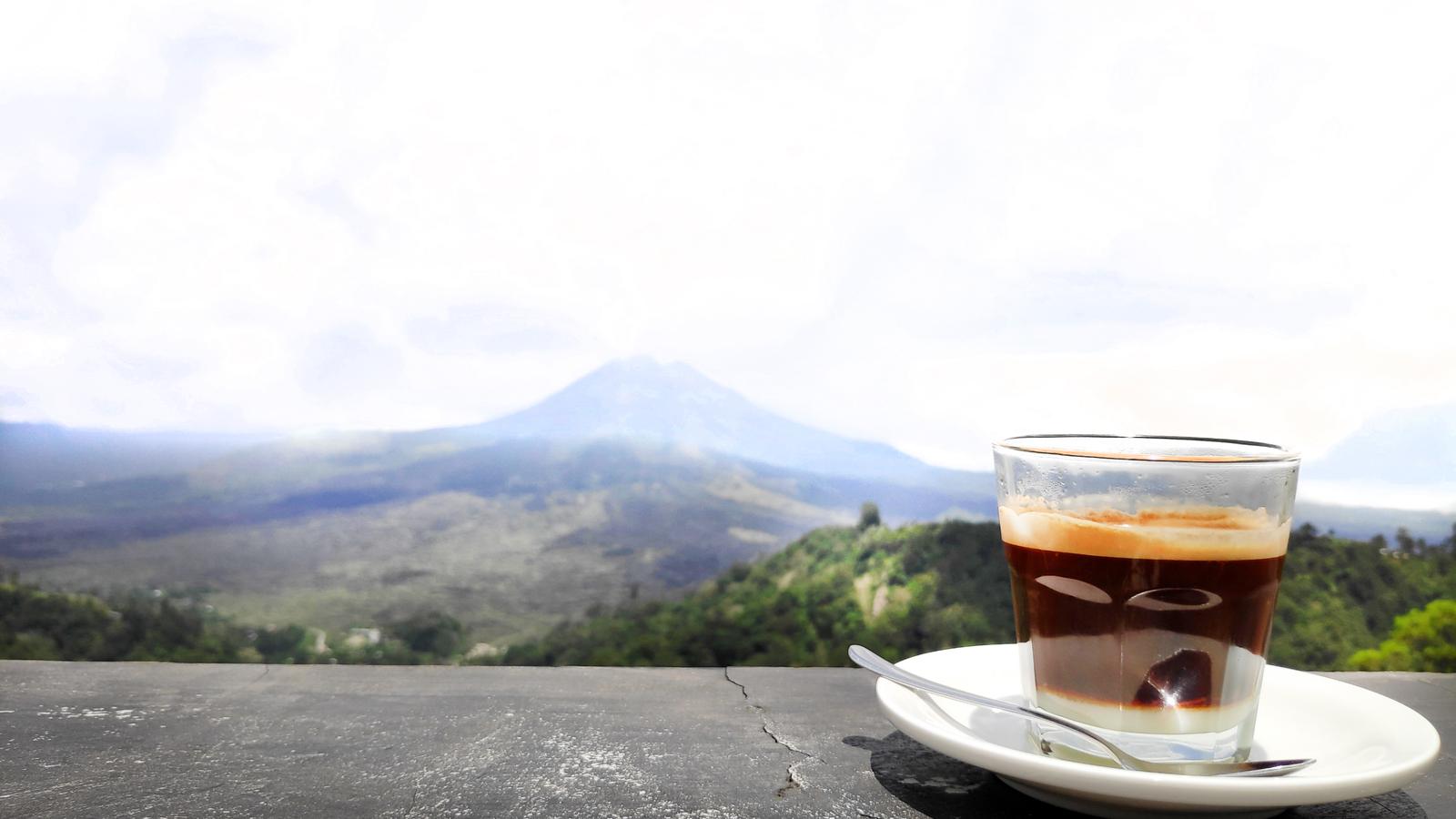A glass of coffee on a stone ledge overlooking Mount Batur