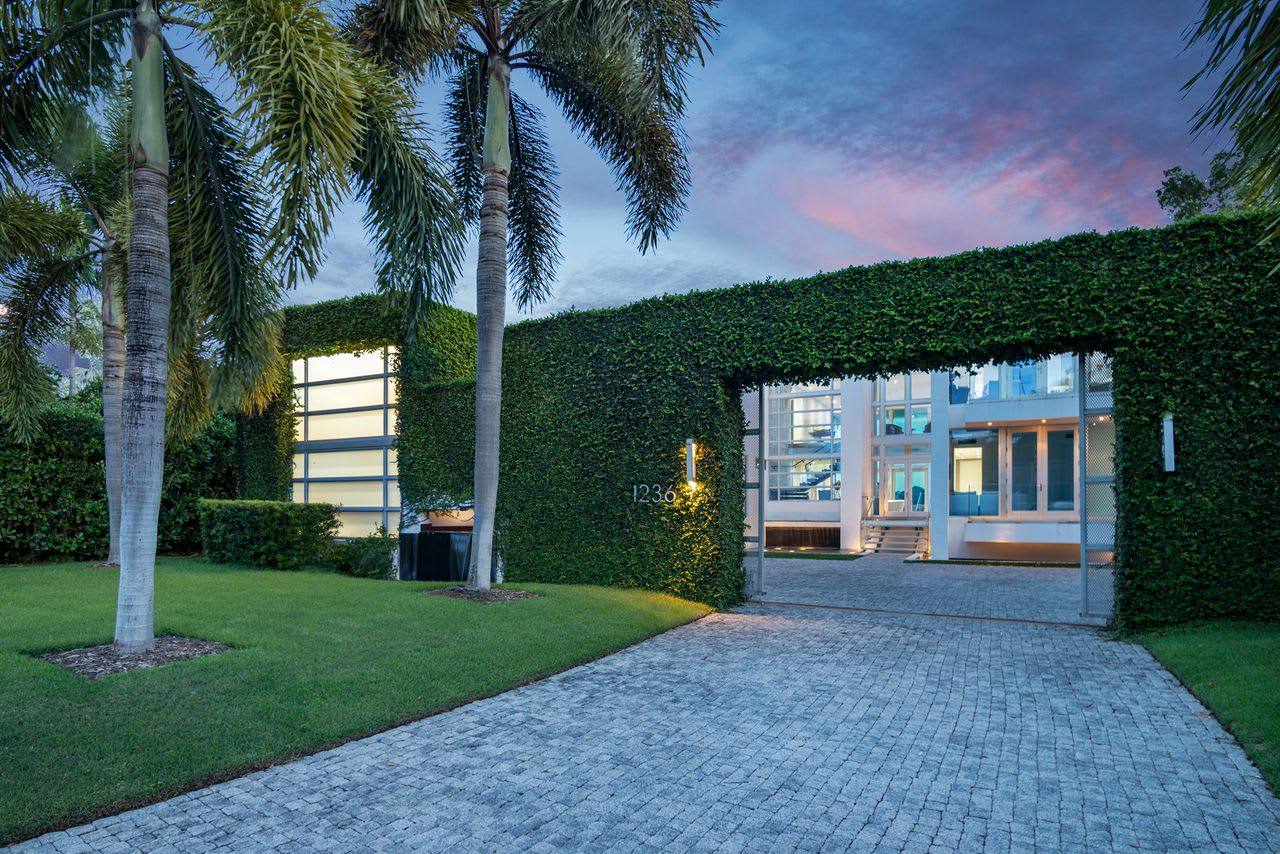 A contemporary Miami house behind a tall hedge at dusk