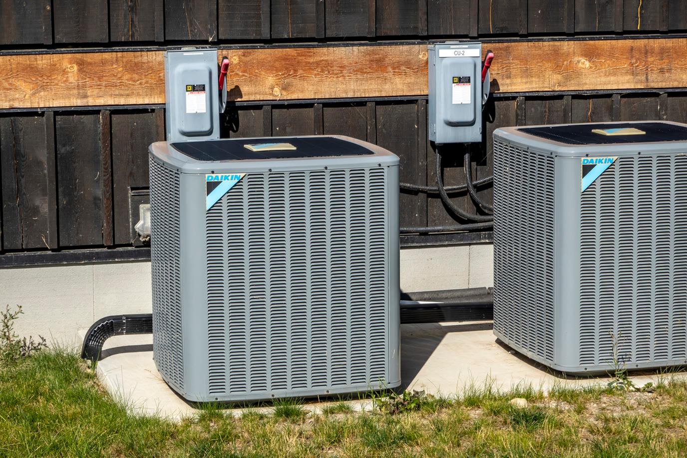 Two Daikin outdoor air conditioning condensers installed side by side on a concrete pad beside a home
