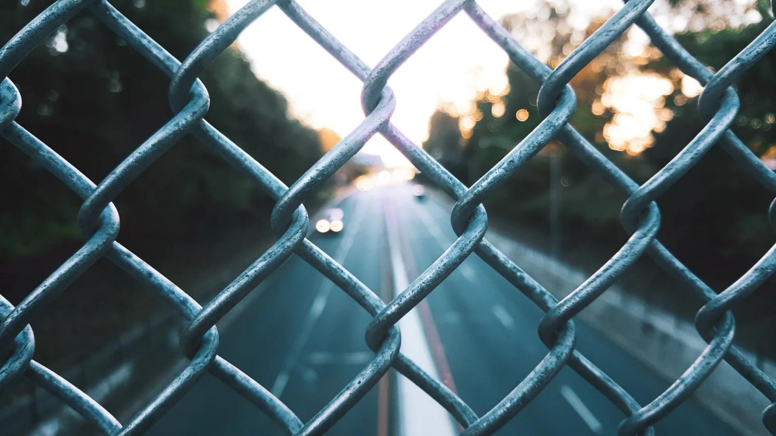 Highway traffic seen through a chain-link fence